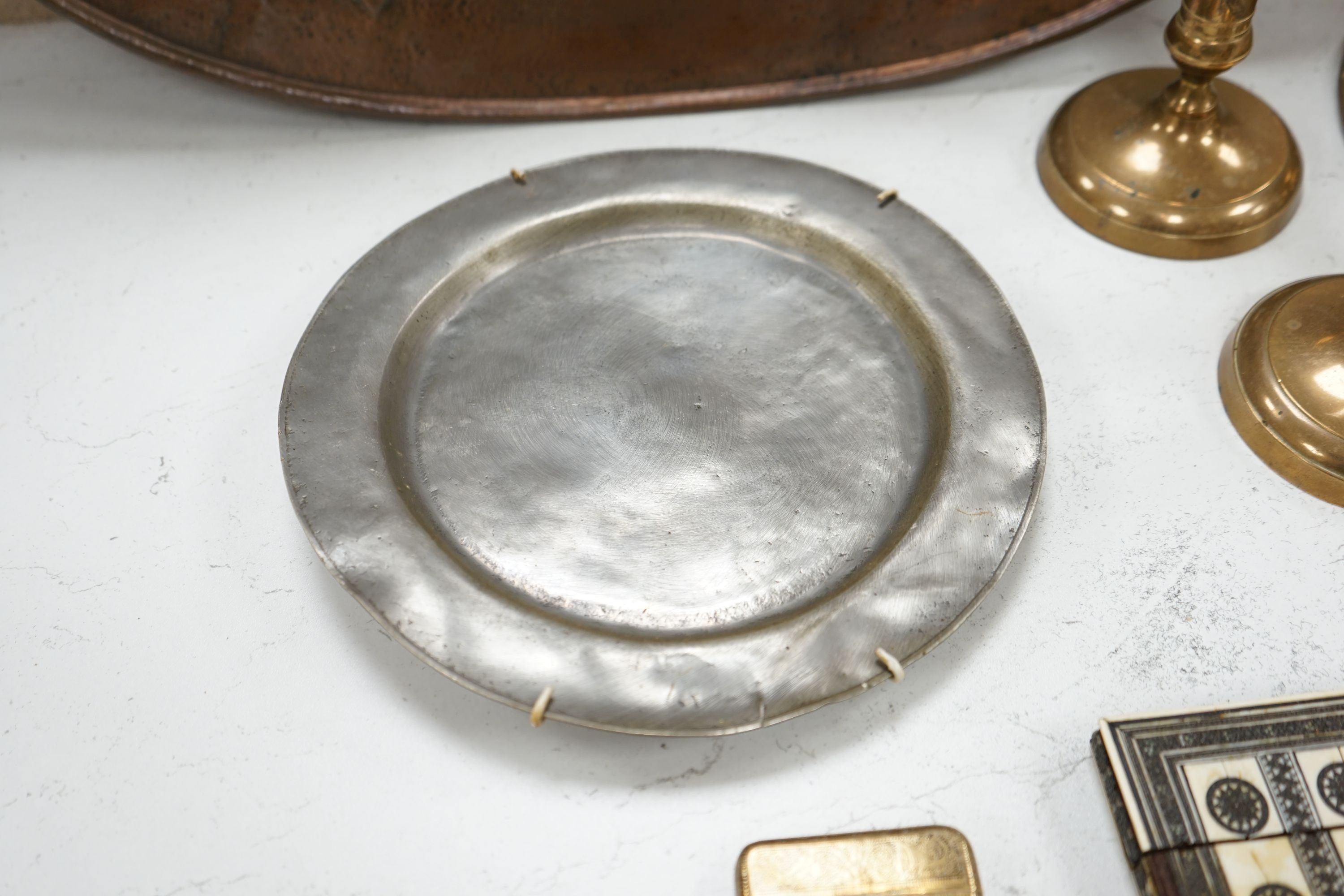 An embossed brass lamp, lustre drop wall light, a pair of bell-metal candlesticks, an 18th century pewter plate and a large Swedish embossed plaque